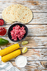 Wall Mural - Cooking Mexican taco ingredients with minced organic meat, corn, calsa over white textured wooden table, top view with space for text.