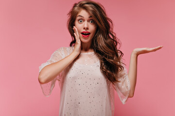 Wall Mural - Shocked woman in white dress looks into camera. Surprised girl on romantic outfit poses on pink isolated background.