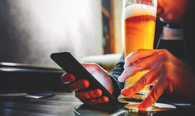 close up of man hand hold smartphone, drinking beer and reading message at bar or pub
