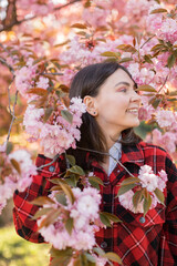 Outdoor portrait of young beautiful Caucasian teen girl smiling and looking into camera, blossom par full of cherry trees on a windy day. 4K footage with sunlight rays