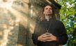 © M-Production - Christian priest with cross standing by the church.