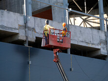 An Aerial Platform Lifts Workers To The Upper Floors Of A Building Under Construction. Background With A Construction Site For Industry, Business.