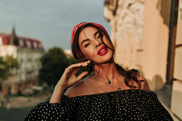 Wall Mural - Modern bright lady with beautiful makeup, pink headband and white manicure in polka dot black shirt looking into camera on balcony..