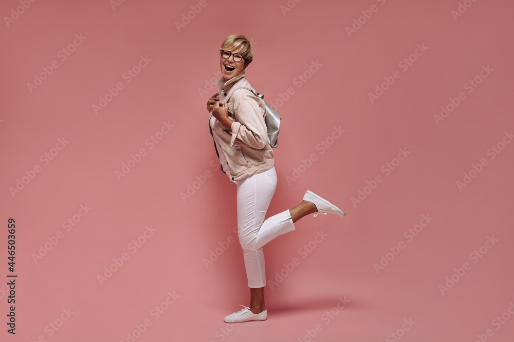 Exciting woman with blonde hair and cool glasses in white trousers and stylish jacket laughing on isolated pink background.. - obrazy, fototapety, plakaty 