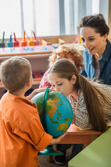 curious girl looking at globe near children and blurred teacher in classroom