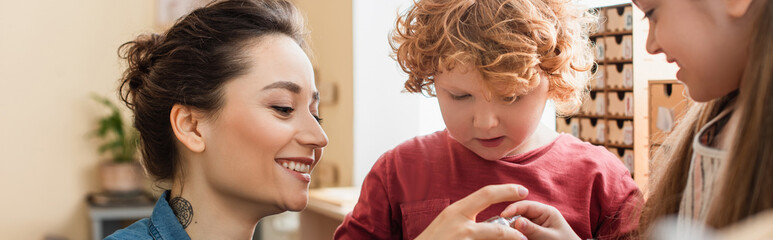 Wall Mural - happy teacher near curly boy and blurred girl in montessori school, banner