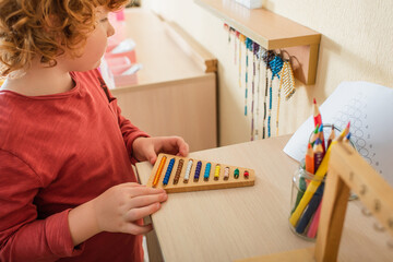 Wall Mural - cropped view of kid playing multicolored beads game near blurred color pencils