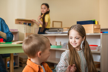 Wall Mural - children talking in classroom near teacher and asian girl on blurred background