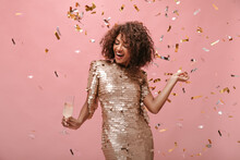 Young Lady With Short Brunette Hair In Shiny Stylish Dress Posing With Glass With Wine And With Confetti On Isolated Backdrop..
