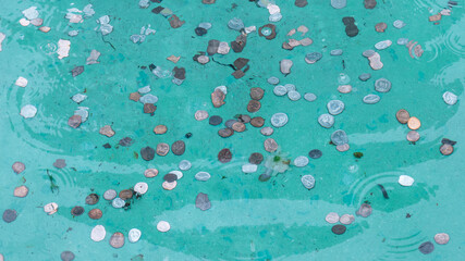 Wishing well pond coin fountain filled with money and spare change reflecting in rippling water background. Luck and finance wealth concept