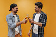 © Look! - Good-humored brunet friends in checkered shirts clink beer bottles on orange background. Cheerful guys smile.