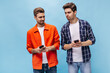 © Look! - Brunet man in checkered shirt tries to watch at his friends phone screen. Guy in orange jacket poses in bad mood.