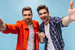 © Look! - Handsome man in orange jacket and his friend in checkered shirt smile and take selfie in good mood on blue background.