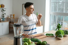 Young man with fresh vegetables for preparing green smoothie in kitchen