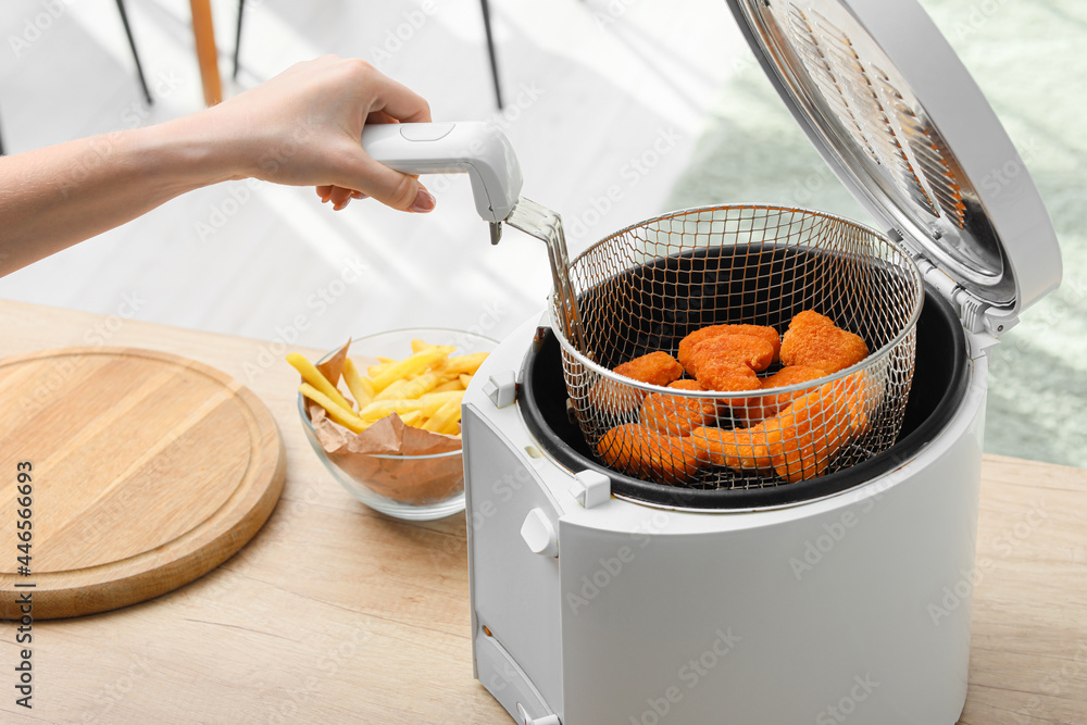 Young woman taking tasty nuggets from deep fryer in kitchen