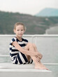 Teen girl 9 years sitting on the parapet by sea and mountains. Summer evening