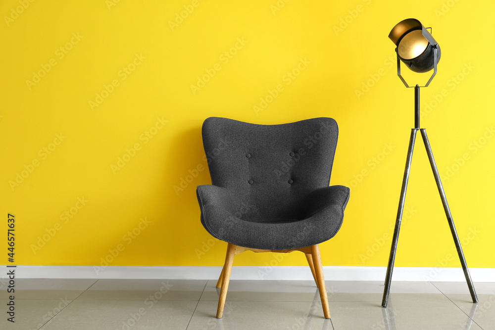 Modern armchair and glowing lamp near color wall