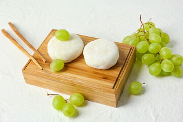 Board with tasty Japanese mochi and grapes on white background