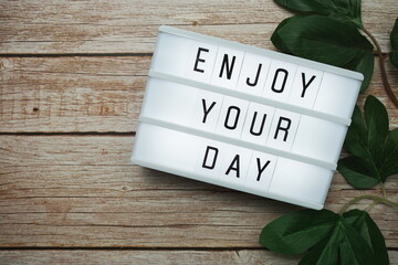 Wall Mural - enjoy your day text on lightbox on wooden background