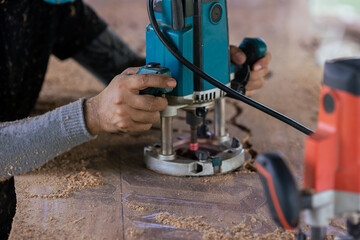 Selective focus. Closeup hand of carpenter use electric trimmer carved on the wooden. Craftsman carving wood in workshop.