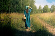 young woman in folk peasant clothes with a wicker basket walks along a field road
