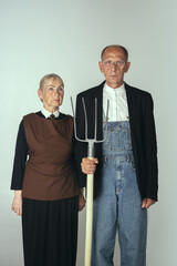 Elderly man and woman in art performance, replica of painting american gothic. Retro style, comparison of eras and cultural concept.