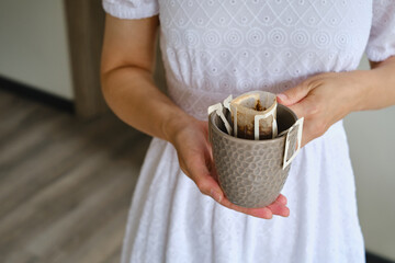 Girl holds a cup with freshly brewed drip coffee. A trendy variety of drip coffee. Hands of the girl in the frame, close-up with a cup of filter coffee in the kitchen. Morning coffee ritual