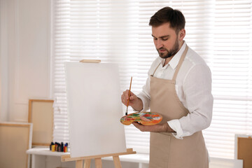 Poster - Young man painting on easel with brush in artist studio