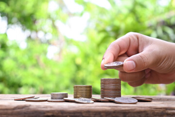 Wall Mural - Human hands holding coins and piles of coins on wooden floor financial and investment ideas.