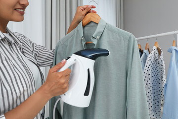 Canvas Print - Woman steaming shirt on hanger at home, closeup