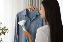 Woman Steaming Shirt On Hanger At Home