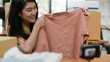 © sarawutnirothon - A woman holding a shirt taking a selfie to live online selling, selling online.