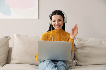 Sticker - Woman with laptop and headphones sitting on sofa at home