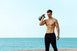 muscular concentrated young sportsman outdoors on the beach doing exercises on the forearms with dumbbells