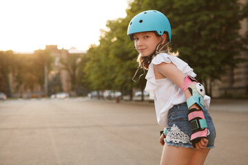 young cheerful girl smiling to the camera over her shoulder while rollerblading, wearing protective 