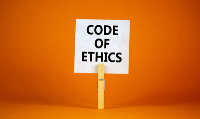 Code of ethics symbol. White paper with words 'Code of ethics', clip on wood clothespin. Beautiful orange background. Business and code of ethics concept. Copy space.