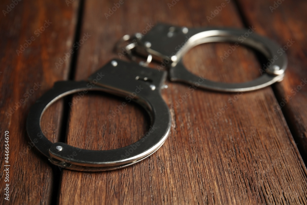 Classic chain handcuffs on wooden table, closeup - obrazy, fototapety, plakaty 