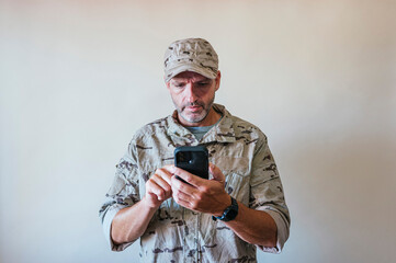 Canvas Print - Caucasian man in camouflaged army uniform using a smart phone, technology concept.