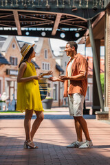 Wall Mural - side view of stylish interracial couple talking on city street