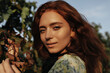 © Look! - Portrait of charming lady with freckles and foxy wavy hairstyle in green clothes smiling and looking into camera outdoor..