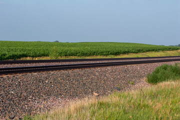 Landscape view of a double railroad track in a rural agricultural landscape on a sunny day, with fields in the background