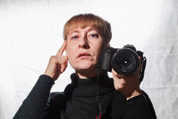 Female photographer in a studio in black dress with camera on white background. Woman posing indoors with cam