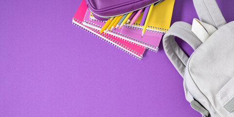 Backpack with colorful school supplies on purple background. Back to school. Flat lay, top view, copy space