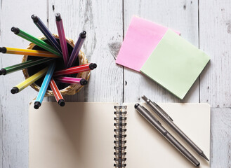 Pen colorful array circular in box with open notebook blank with two silver pen on white wood table with note paper and nature light of sun idea concept top view,business and education