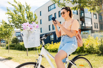 Poster - people, leisure and lifestyle - happy young woman with smartphone, backpack and flowers in basket of bicycle on city street