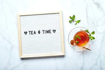 Wall Mural - Tea time. White letter board with text on marble table with glass cup of tea with mint leaves