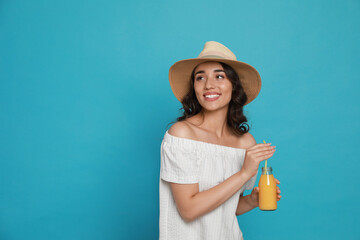 Canvas Print - Beautiful young woman with straw hat and bottle of refreshing drink on light blue background. Space for text