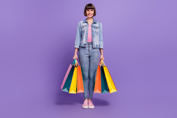 Wall Mural - Full size photo of young cute brunette lady hold bags wear spectacles jeans shirt isolated on purple background