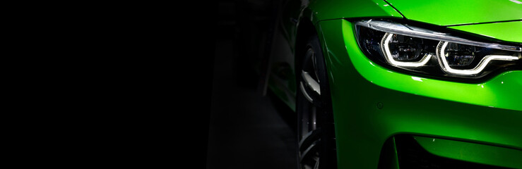 Front headlights of green modern sport car on black background, free space on left side for text.