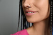 Young woman with nose piercing on grey background, closeup
